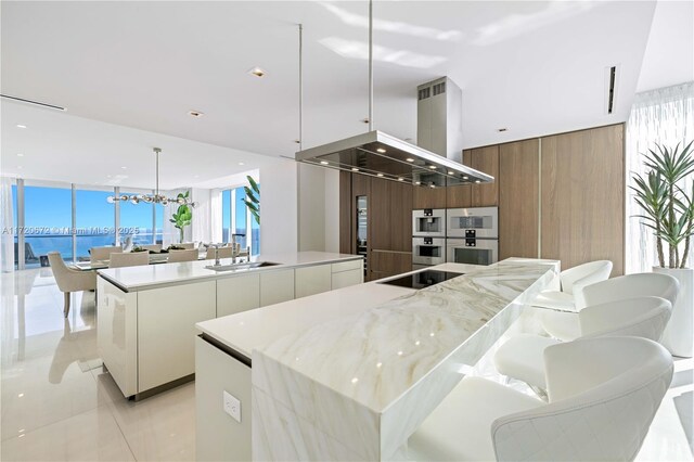 kitchen with island range hood, a spacious island, sink, a water view, and white cabinetry