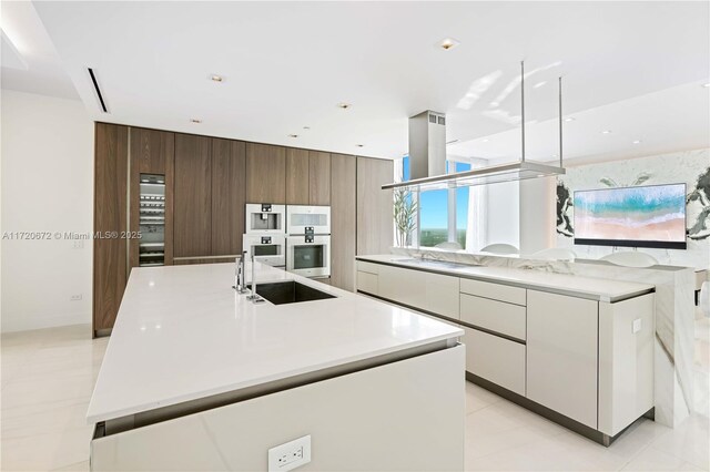 kitchen with sink, white cabinets, wooden walls, a kitchen island with sink, and double wall oven