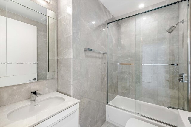 bathroom featuring vanity, tile walls, and bath / shower combo with glass door