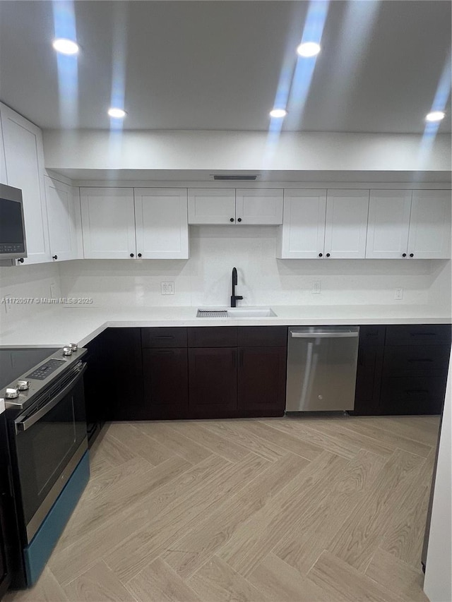 kitchen with decorative backsplash, stainless steel appliances, light parquet floors, sink, and white cabinetry