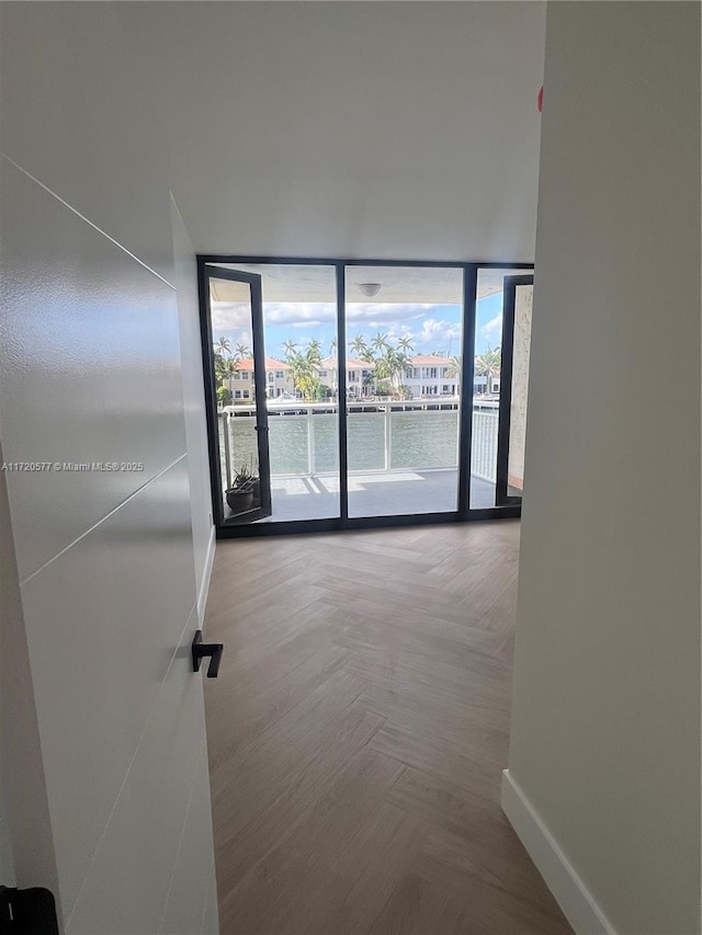 spare room featuring a wall of windows, a water view, and parquet flooring