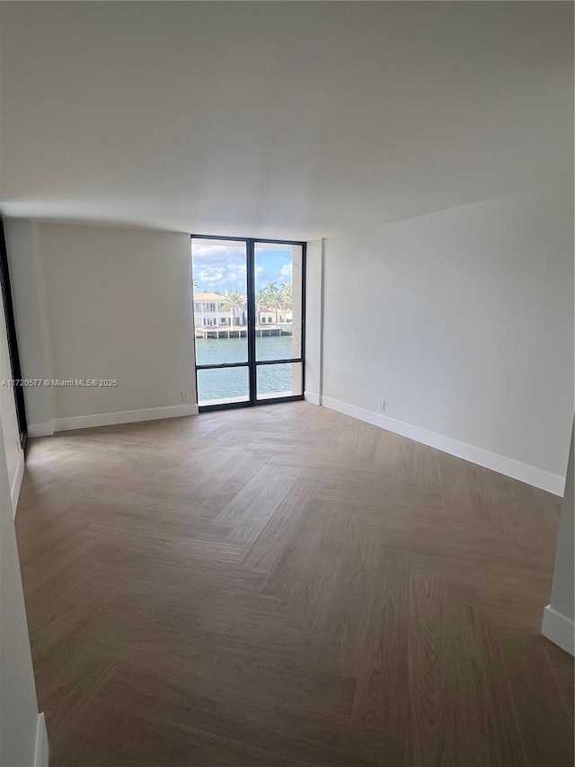 empty room featuring expansive windows, a water view, and parquet flooring