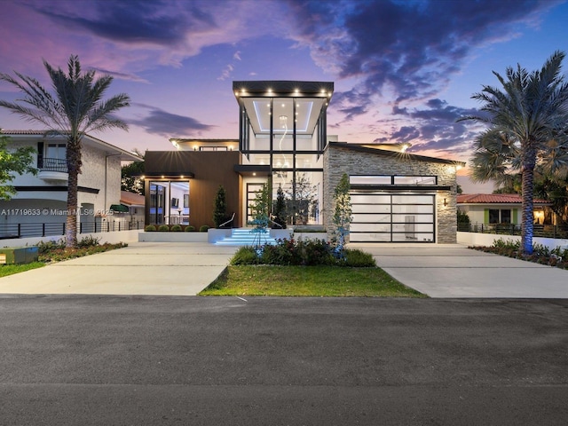 contemporary house with a garage, stone siding, concrete driveway, and stucco siding