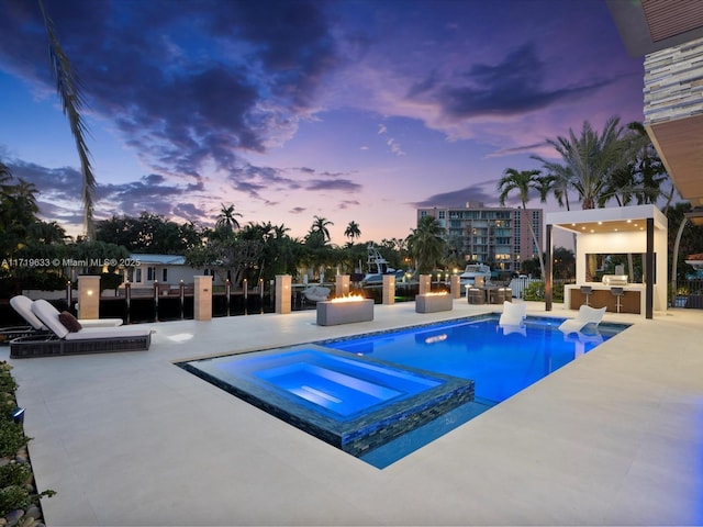 pool at dusk with a pool with connected hot tub, outdoor dry bar, a patio, and area for grilling