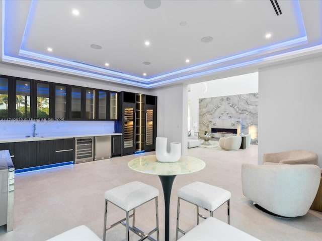 interior space with a tray ceiling, wine cooler, a sink, and a high end fireplace