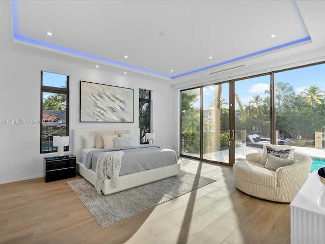 bedroom featuring access to outside, a tray ceiling, multiple windows, and light wood-type flooring