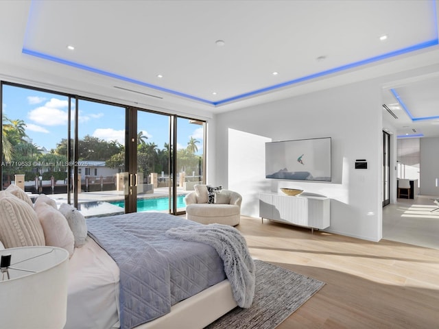 bedroom featuring recessed lighting, light wood-type flooring, a raised ceiling, and access to exterior