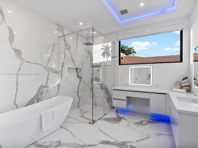 full bathroom featuring a freestanding tub, a sink, a marble finish shower, double vanity, and a raised ceiling