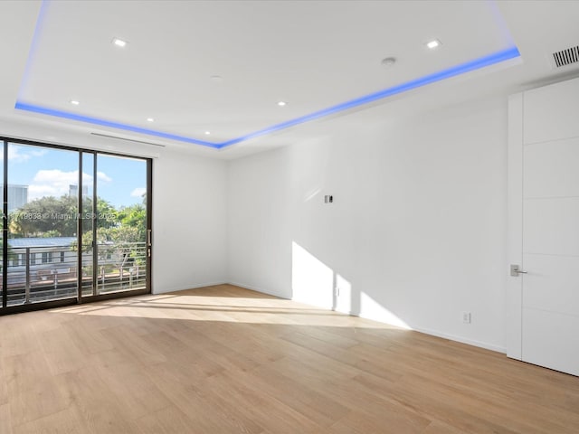 unfurnished room with a tray ceiling, floor to ceiling windows, visible vents, and light wood-style flooring