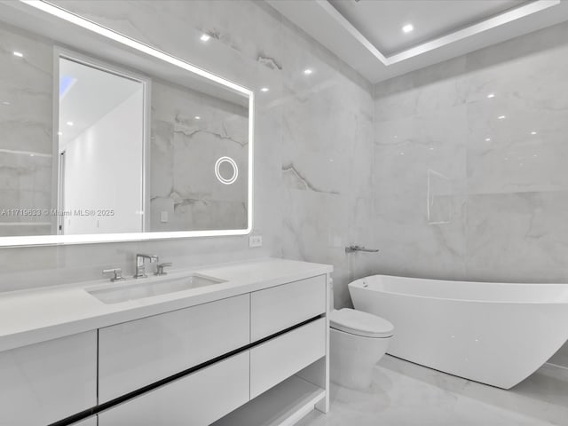 full bathroom featuring toilet, vanity, tile walls, marble finish floor, and a soaking tub