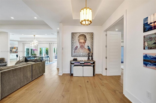 corridor featuring a raised ceiling, an inviting chandelier, and light hardwood / wood-style floors