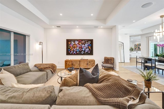 living room featuring a notable chandelier, light hardwood / wood-style floors, and a raised ceiling