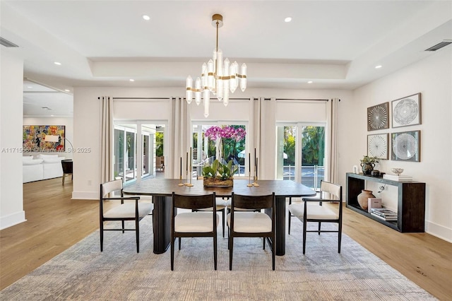 dining space with an inviting chandelier, a tray ceiling, and light hardwood / wood-style flooring