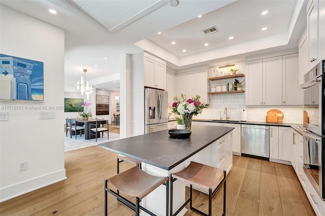 kitchen featuring a kitchen breakfast bar, stainless steel appliances, a raised ceiling, and white cabinets