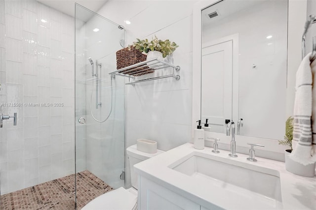 bathroom with vanity, toilet, a shower with shower door, and tile walls