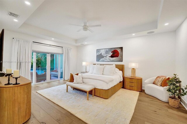 bedroom featuring access to exterior, a tray ceiling, light hardwood / wood-style flooring, and ceiling fan