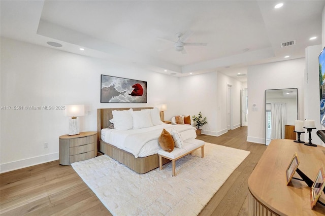 bedroom featuring a tray ceiling, light hardwood / wood-style flooring, high end refrigerator, and ceiling fan