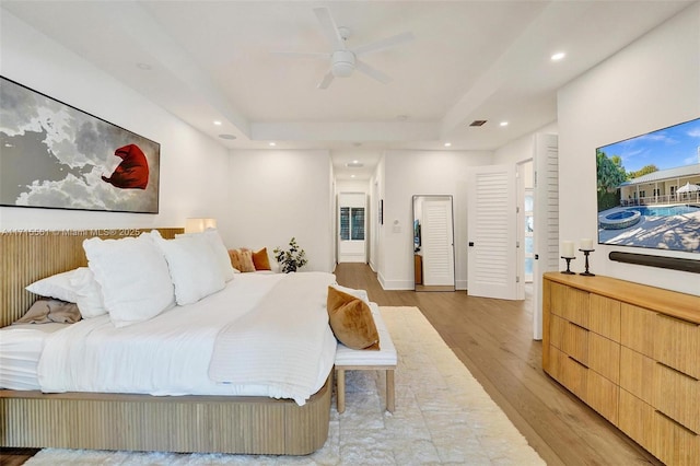 bedroom with ceiling fan, light hardwood / wood-style floors, and a tray ceiling