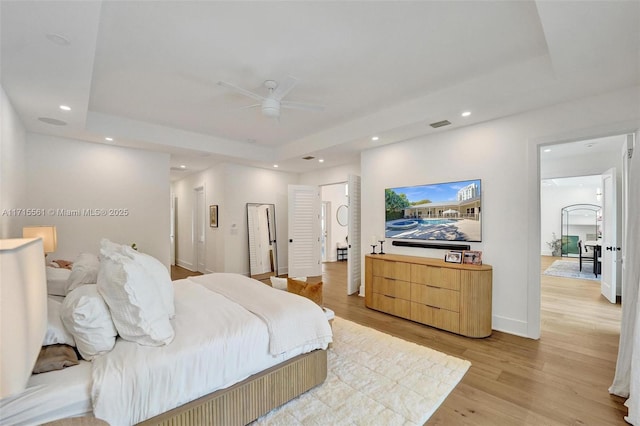 bedroom featuring a tray ceiling, light hardwood / wood-style floors, and ceiling fan