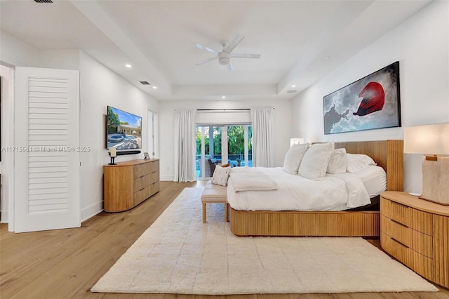 bedroom featuring access to exterior, a tray ceiling, hardwood / wood-style floors, and ceiling fan