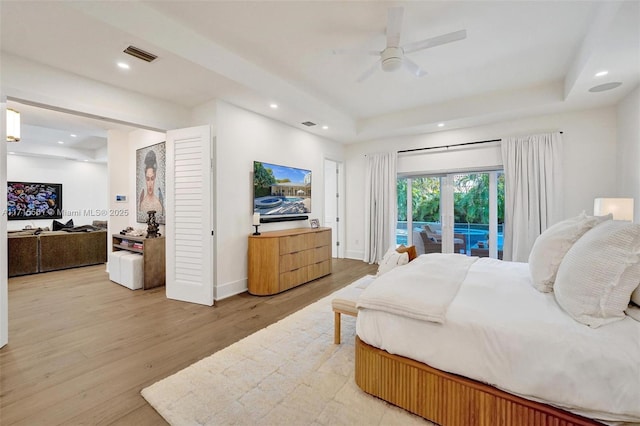 bedroom featuring ceiling fan, a tray ceiling, light hardwood / wood-style flooring, and access to outside