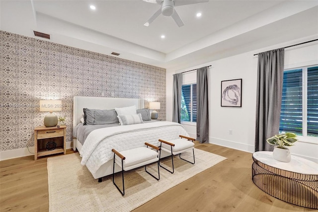 bedroom with a raised ceiling, wood-type flooring, ceiling fan, and multiple windows