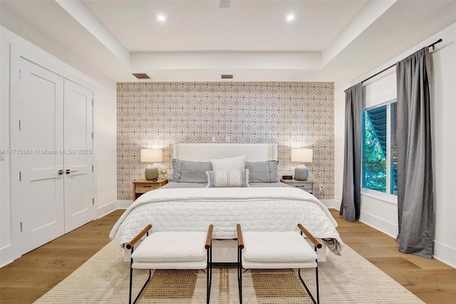 bedroom featuring a raised ceiling, a closet, and light hardwood / wood-style flooring