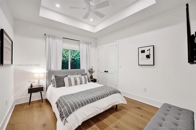 bedroom featuring hardwood / wood-style floors, a closet, a raised ceiling, and ceiling fan