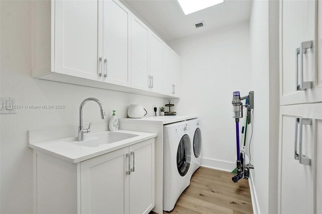 clothes washing area with sink, cabinets, a skylight, light hardwood / wood-style flooring, and washer and clothes dryer