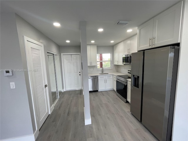 kitchen featuring sink, light wood-type flooring, tasteful backsplash, white cabinetry, and stainless steel appliances