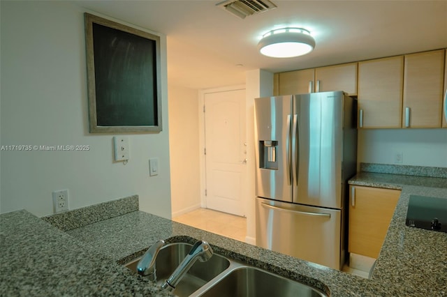 kitchen featuring stone counters, stainless steel refrigerator with ice dispenser, black stovetop, and sink