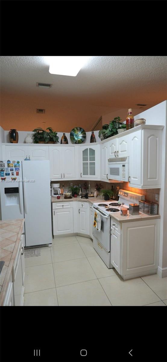 kitchen with white cabinetry, tile counters, backsplash, white appliances, and light tile patterned floors