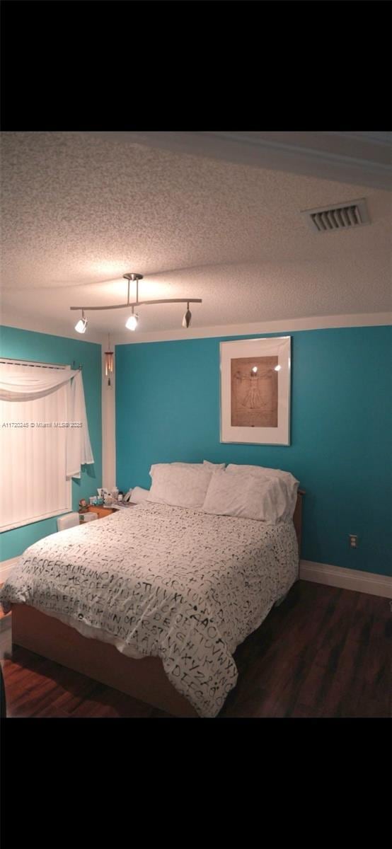 bedroom featuring dark hardwood / wood-style floors, a textured ceiling, and track lighting