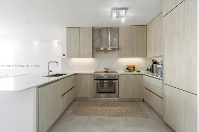 kitchen with light brown cabinetry, wall chimney exhaust hood, sink, black electric stovetop, and oven