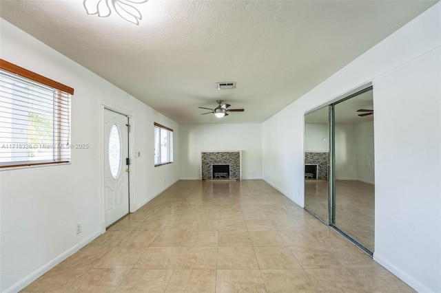 unfurnished living room with ceiling fan, a textured ceiling, a fireplace, and visible vents