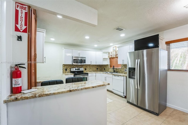 kitchen with a peninsula, light stone countertops, stainless steel appliances, white cabinetry, and a sink