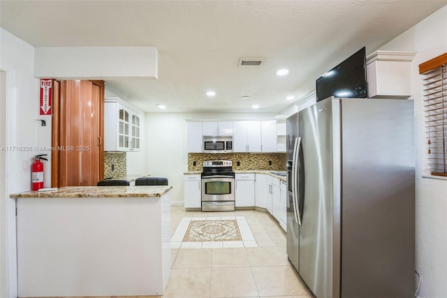 kitchen featuring light stone counters, stainless steel appliances, glass insert cabinets, white cabinetry, and a peninsula