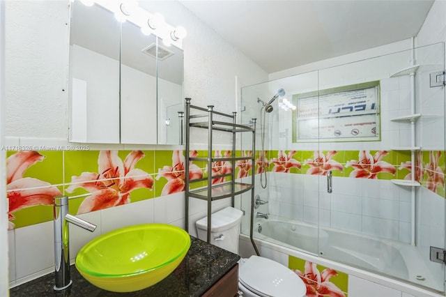 bathroom featuring tiled shower / bath, visible vents, a textured wall, toilet, and vanity