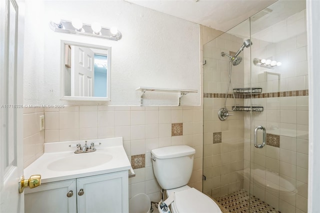 full bath featuring toilet, vanity, tile walls, wainscoting, and a shower stall