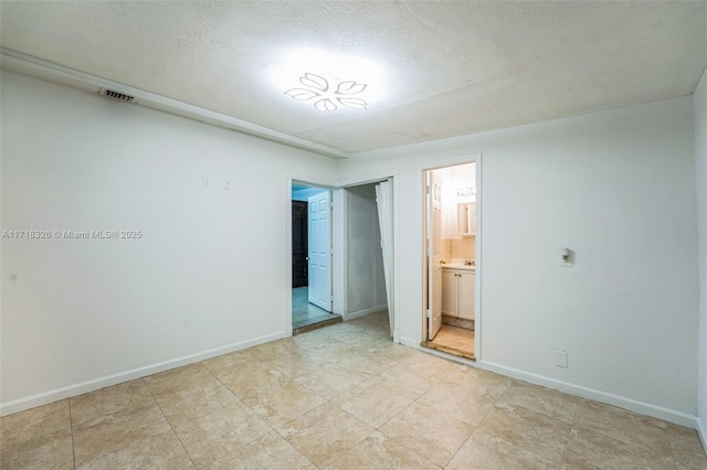 unfurnished bedroom featuring a textured ceiling, connected bathroom, visible vents, and baseboards