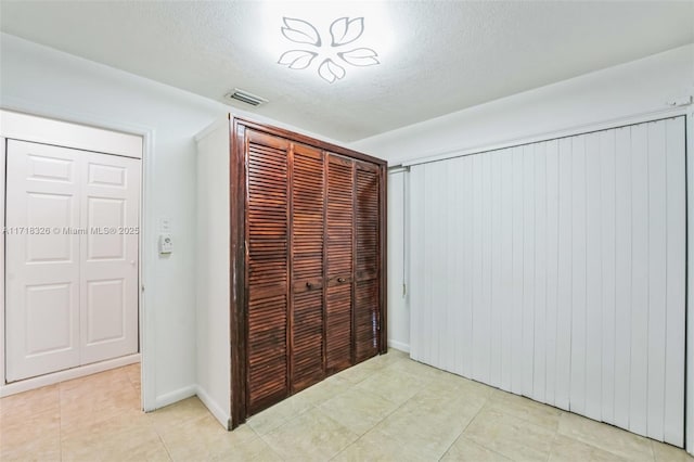 unfurnished bedroom featuring a closet, visible vents, a textured ceiling, and light tile patterned flooring