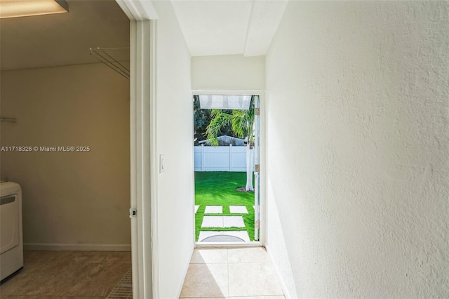 doorway to outside with washer / clothes dryer, light tile patterned flooring, a textured wall, and baseboards