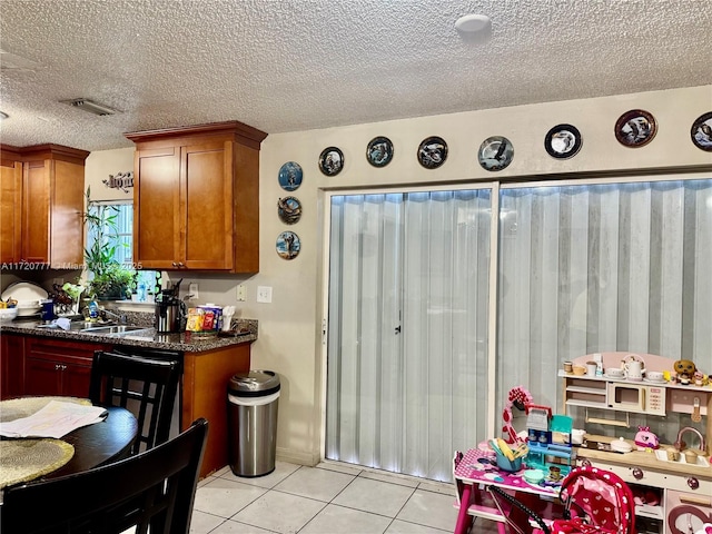 kitchen featuring light tile patterned floors, a textured ceiling, dark stone counters, and sink