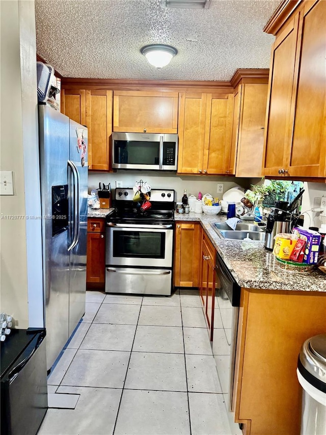 kitchen featuring sink, light stone counters, a textured ceiling, light tile patterned floors, and appliances with stainless steel finishes