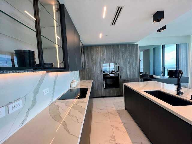 kitchen with wood walls, light stone countertops, black electric cooktop, and sink