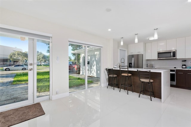 kitchen with an island with sink, appliances with stainless steel finishes, dark brown cabinets, a kitchen bar, and white cabinetry