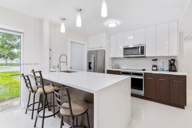 kitchen with appliances with stainless steel finishes, a center island with sink, dark brown cabinets, and sink