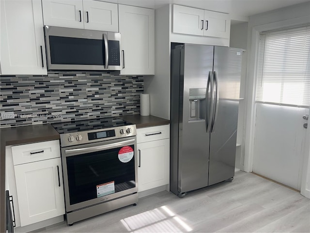 443 NE 195th St Unit 242, Miami, FL 33179 - kitchen featuring stainless steel appliances, light wood-style flooring, dark countertops, backsplash, and white cabinetry