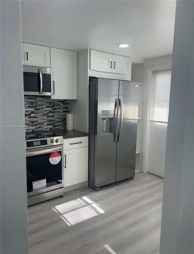 kitchen featuring tasteful backsplash, white cabinets, stainless steel appliances, and light wood-type flooring