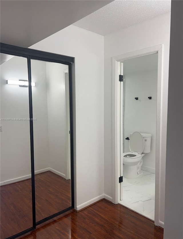 interior space featuring wood-type flooring, a textured ceiling, and toilet